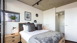 A modern bedroom with a bed, bedside table, and a potted plant by the window. - Stylish 2-bed Apt in Southbank With Parking (Southbank)
