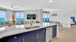 A modern kitchen with a large island, built-in dishwasher, and a dining area with a view of the ocean. - Full Remodel 2023 - 2 Free Sets of Beach Chairs! (Panama City Beach)
