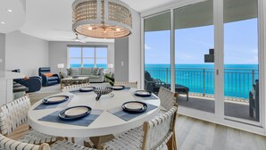 A spacious living area with a round dining table, comfortable seating, and a large sliding glass door leading to a balcony with a view of the ocean. - Full Remodel 2023 - 2 Free Sets of Beach Chairs! (Panama City Beach)