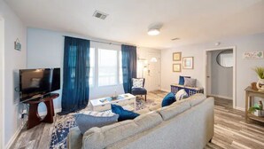 Una sala de estar con sofá, mesa de centro y televisor. Hay una puerta que da a otra habitación.