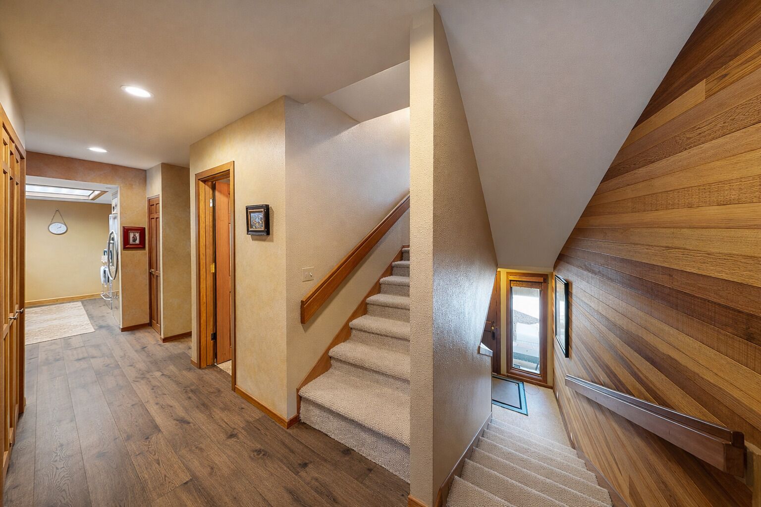 A hallway with wooden flooring, a carpeted staircase, and a wooden wall.