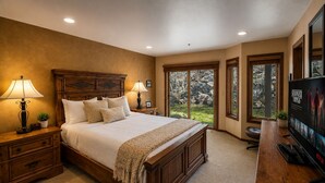 A bedroom with a large bed, wooden headboard, bedside lamps, a TV, and a view of the outdoors. - 1791 Lakeside Getaway At Deer Valley! Outdoor Heated Pool & Hot Tubs! 2 Bedroom Condo by RedAwning (Park City)