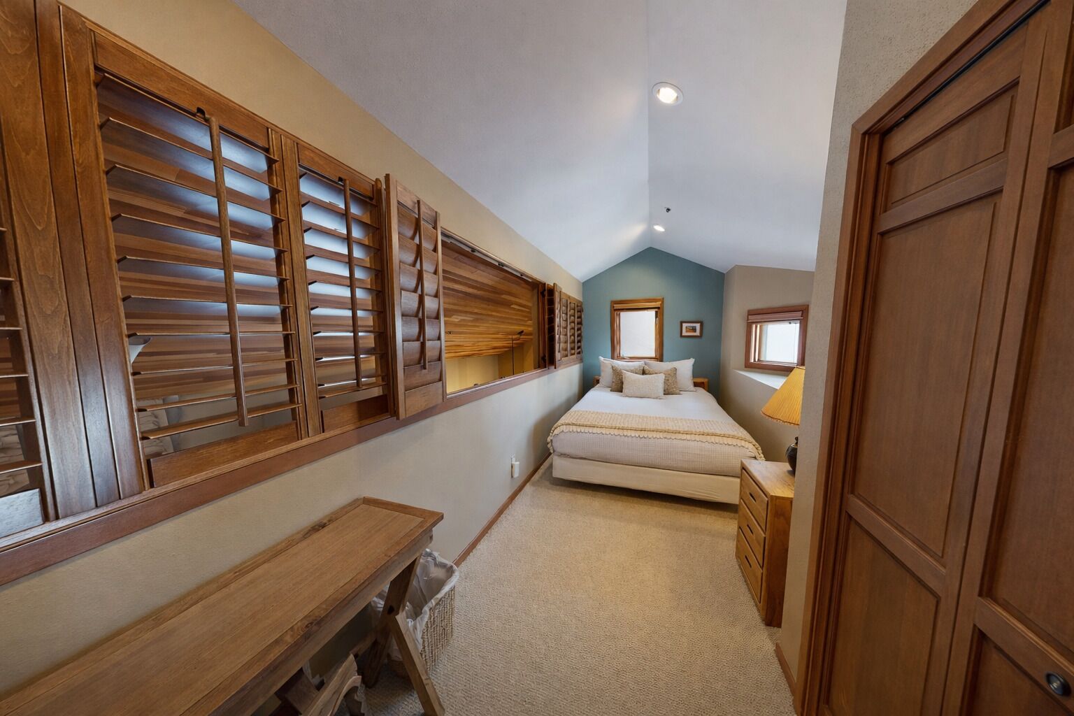 A narrow, sloped room with a bed, a desk, and wooden shutters on the windows.
