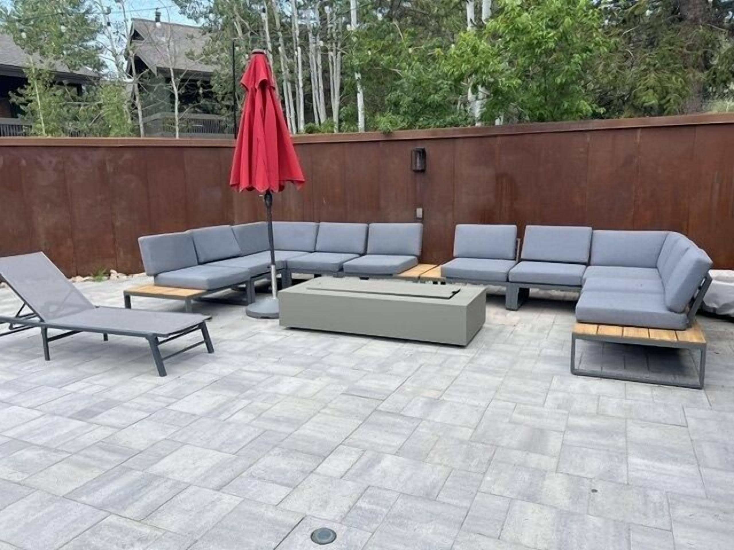 An outdoor seating area with a sectional sofa, lounge chairs, and a red umbrella.