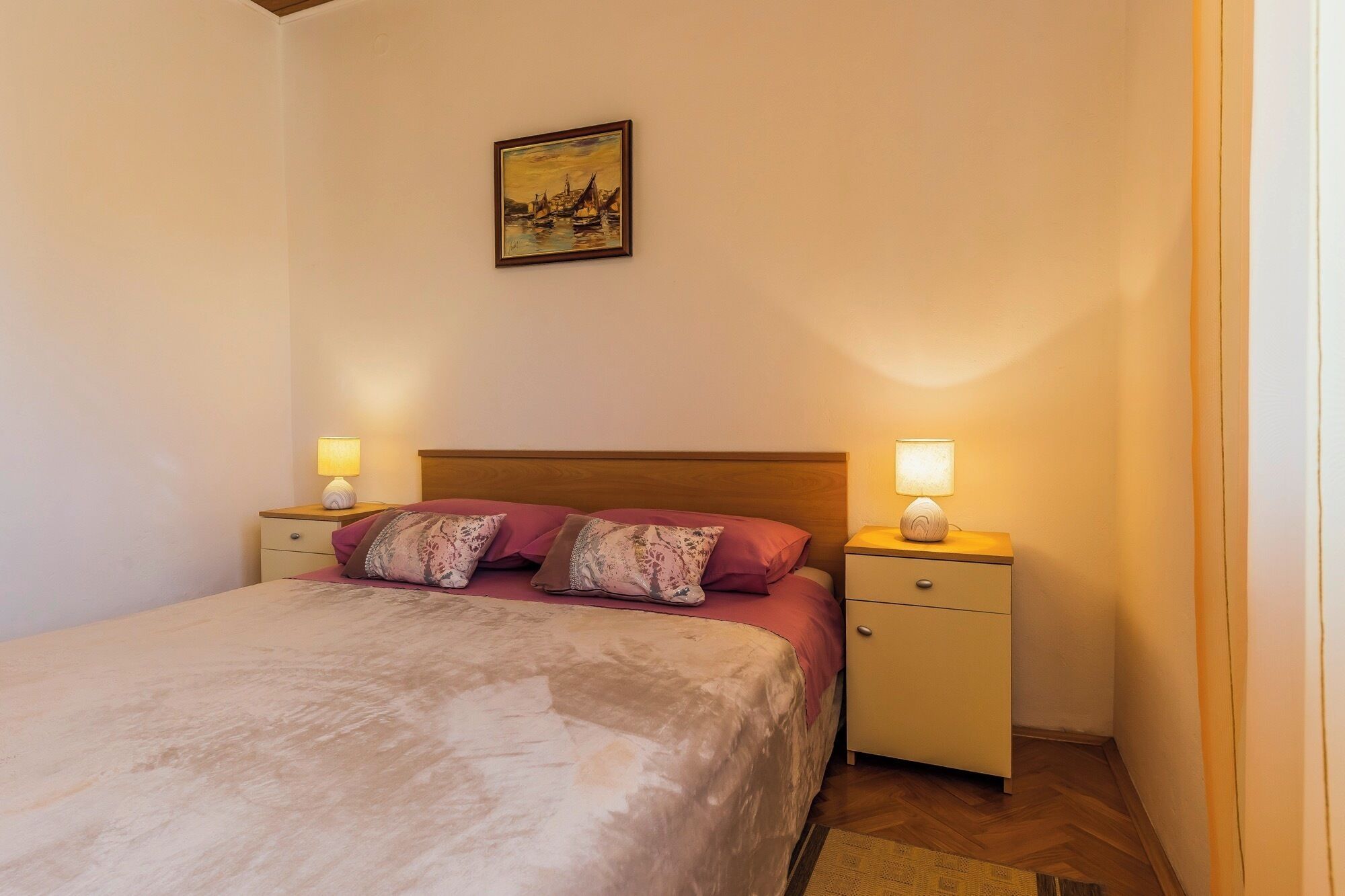 Ein Schlafzimmer mit einem Bett, zwei Nachttischen, einem Wandbild und Holzboden.