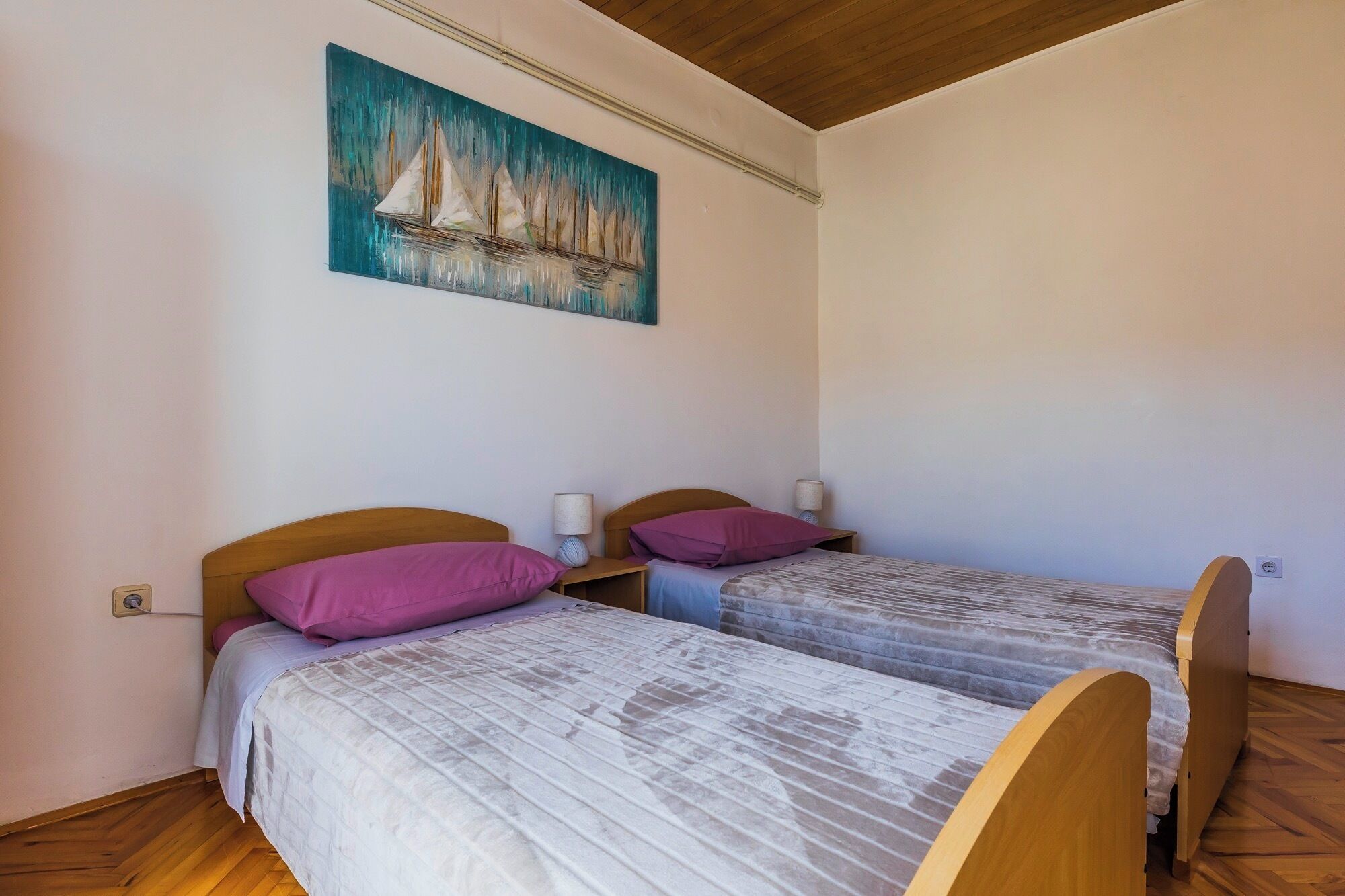 Una habitación con dos camas, cada una con cabecero de madera, un cuadro de veleros en la pared y suelo de madera.