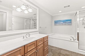 A modern bathroom with a large mirror, two sinks, a bathtub, and wooden cabinets.