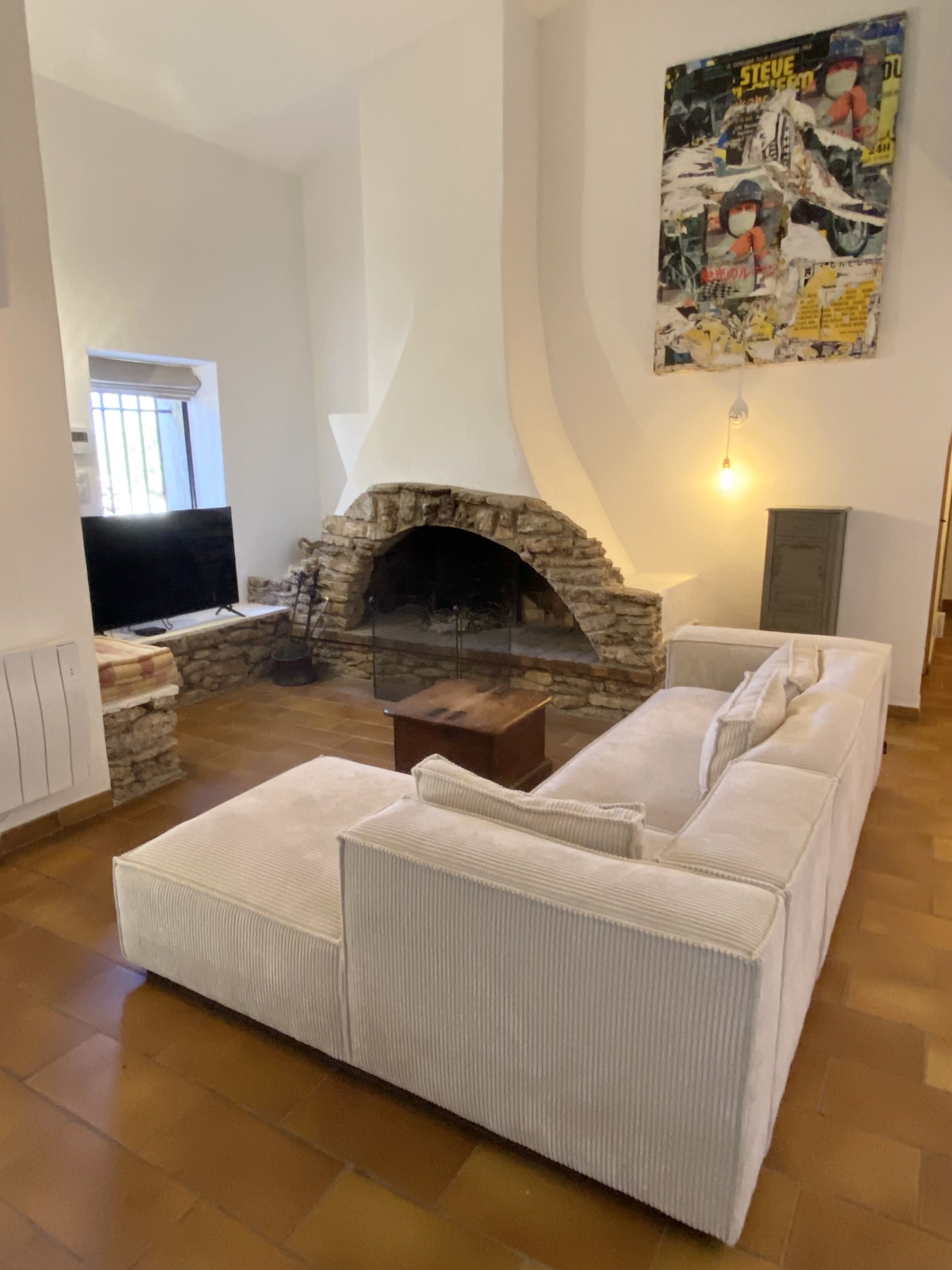 A living room with a stone fireplace, a sofa set, a television, and a poster on the wall.
