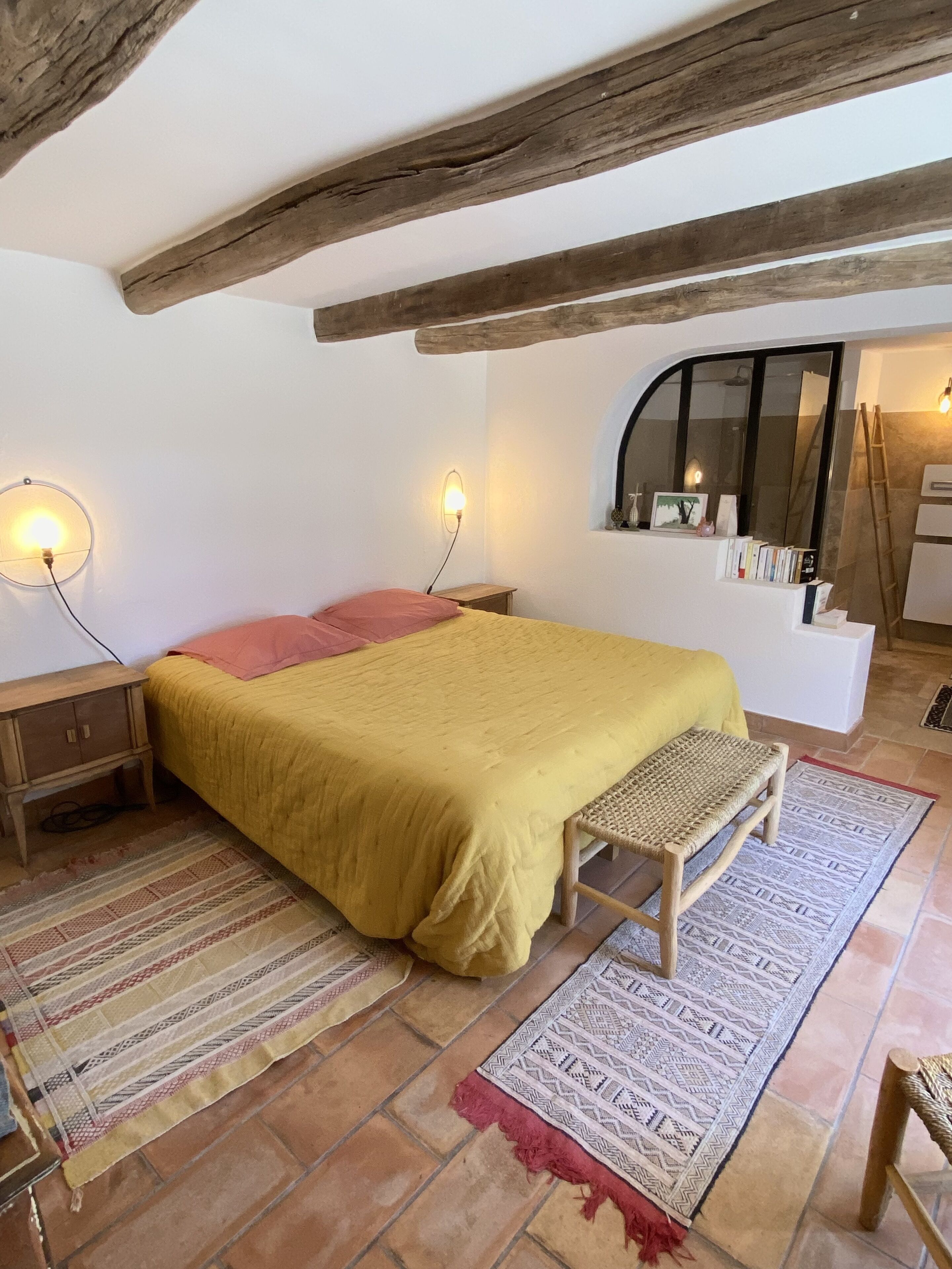 A bedroom with a bed, wooden bench, two bedside tables, a mirror, and a window.