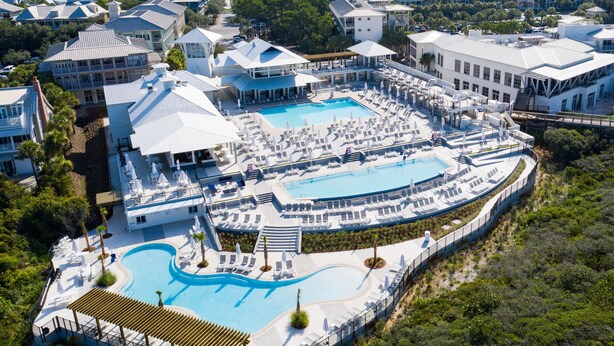 Ett semesterkomplex med en stor pool i mitten, flera områden för solbad och en mängd olika byggnader med distinkta arkitektoniska stilar.