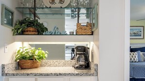 A kitchen with white cabinets, a coffee maker, and a glass shelf with decorative plates and glasses. - Point Emerald E-202, Oceanside Condo in Emerald Isle, NC! (Emerald Isle)