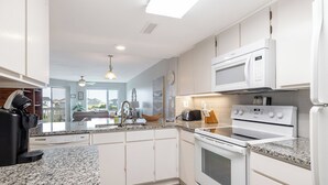 A modern kitchen with white cabinets, granite countertops, a built-in oven, microwave, and a coffee maker. - Point Emerald E-202, Oceanside Condo in Emerald Isle, NC! (Emerald Isle)
