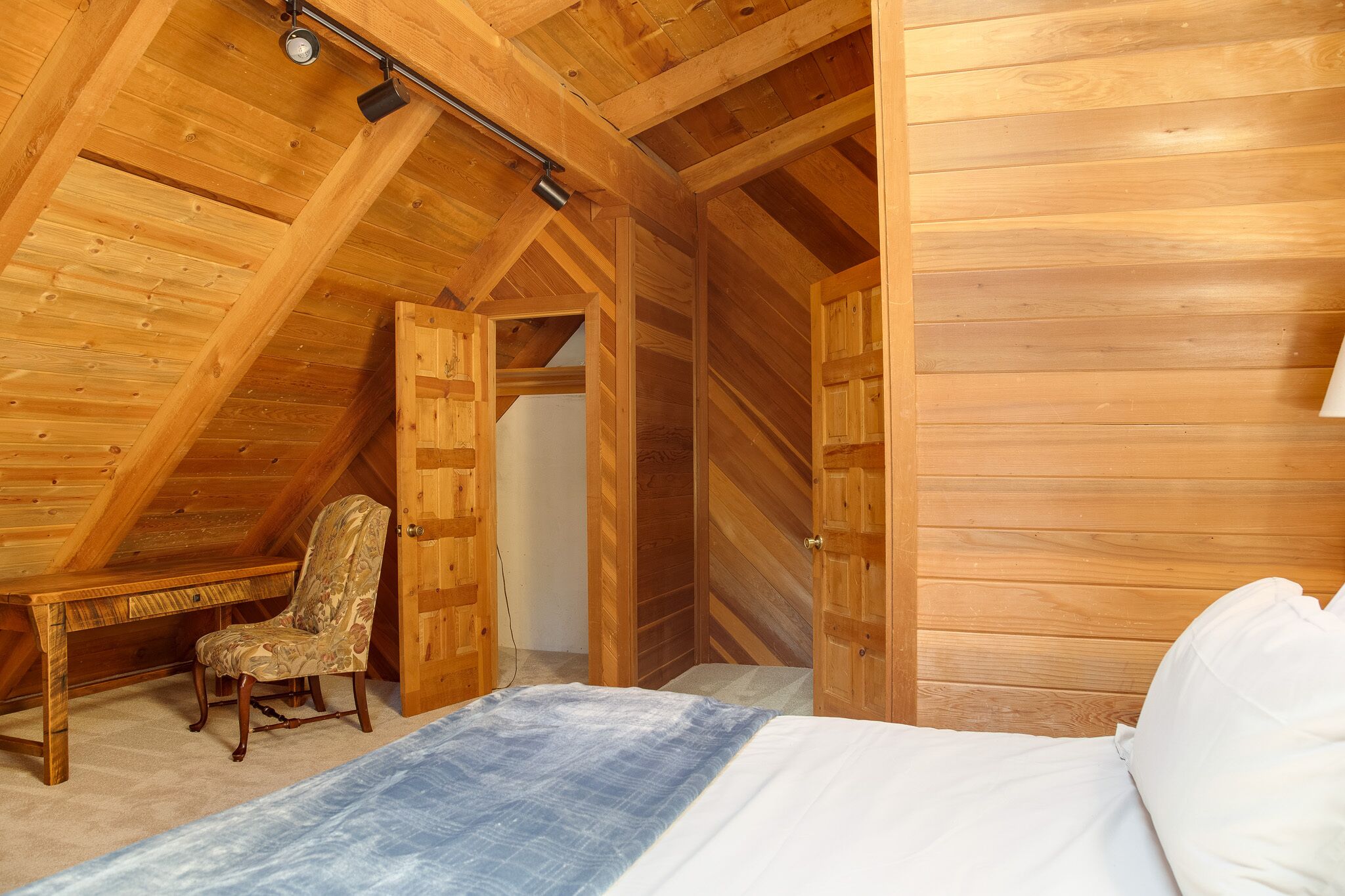 A bedroom with a wooden ceiling, a bed, a chair, and a desk.