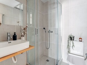 A modern bathroom with a glass-enclosed shower, a white sink with a wooden shelf, and a toilet with a plant and reed diffuser. - Sanders Port - Darling Studio Near Piraeus Port (Piraeus)