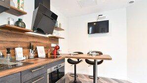 A modern kitchen with a wooden countertop, two black bar stools, a built-in oven, and a flat-screen TV mounted on the wall.
