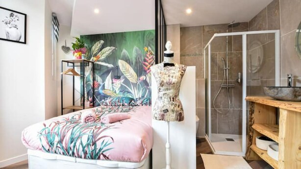 A bedroom with a bed, a mannequin, a shower, and a bathroom vanity.