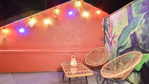 A rooftop terrace with string lights, two wicker chairs, a small table, and a mural.