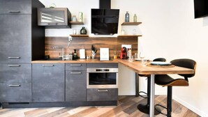 A modern kitchen with dark cabinetry, a wooden countertop, a built-in oven, and a dining area with a table and chairs.