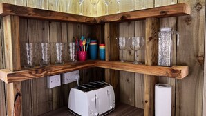 A corner of a room with wooden shelves holding various glassware, a toaster, and a roll of toilet paper.