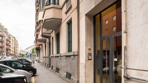 A narrow street with parked cars and a building with a large glass entrance. - The Best Rent - Gorgeous two-bedroom apartment close to Cinque Giornate square (Milano)