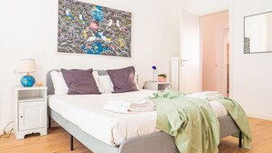 A bedroom with a bed, a nightstand, a lamp, a painting, and a door. - The Best Rent - Apartment close to Porta Romana (Milano)