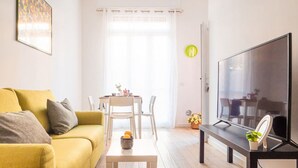 A living room with a yellow sofa, a coffee table, a TV, and a dining area with a table and chairs. - The Best Rent - Apartment close to Porta Romana (Milano)