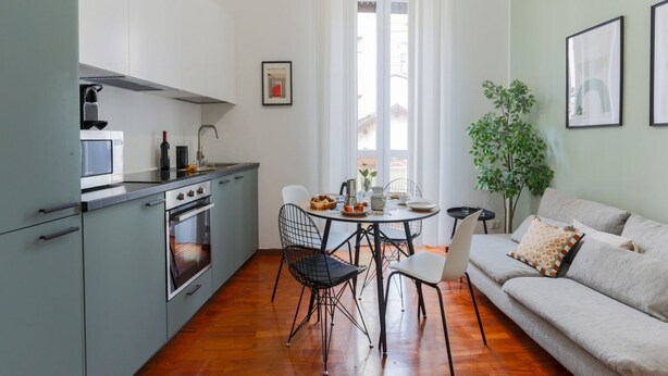 Uma cozinha compacta com eletrodomésticos modernos, uma área de refeições com mesa redonda e cadeiras, e um sofá com almofadas.