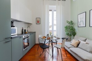 Une cuisine compacte dotée d’appareils électroménagers modernes, un coin repas avec une table ronde et des chaises, et un canapé agrémenté de coussins.