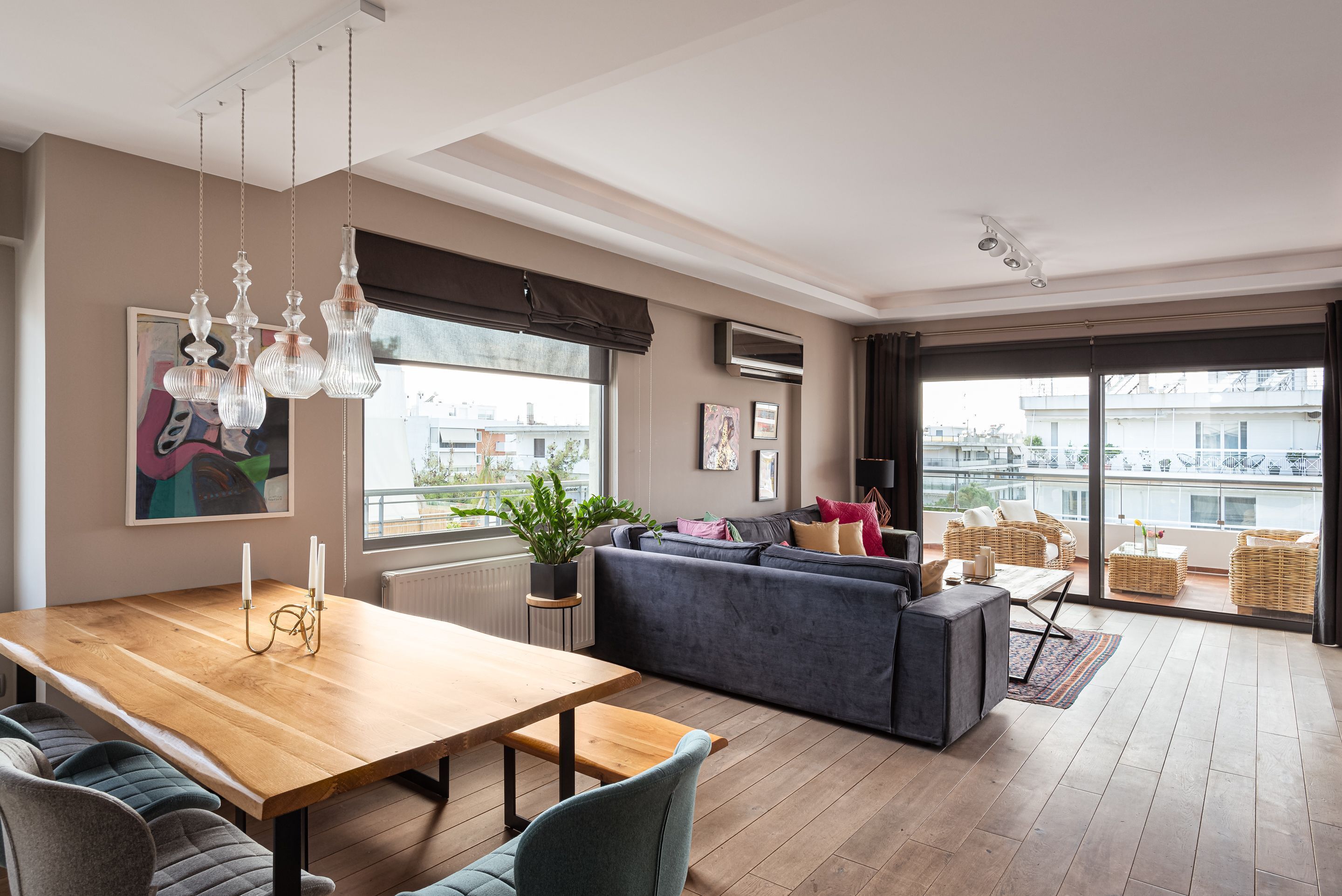 Um espaço de estar moderno com uma mesa de jantar de madeira, sofás cinzentos e uma grande janela com vista para a cidade.