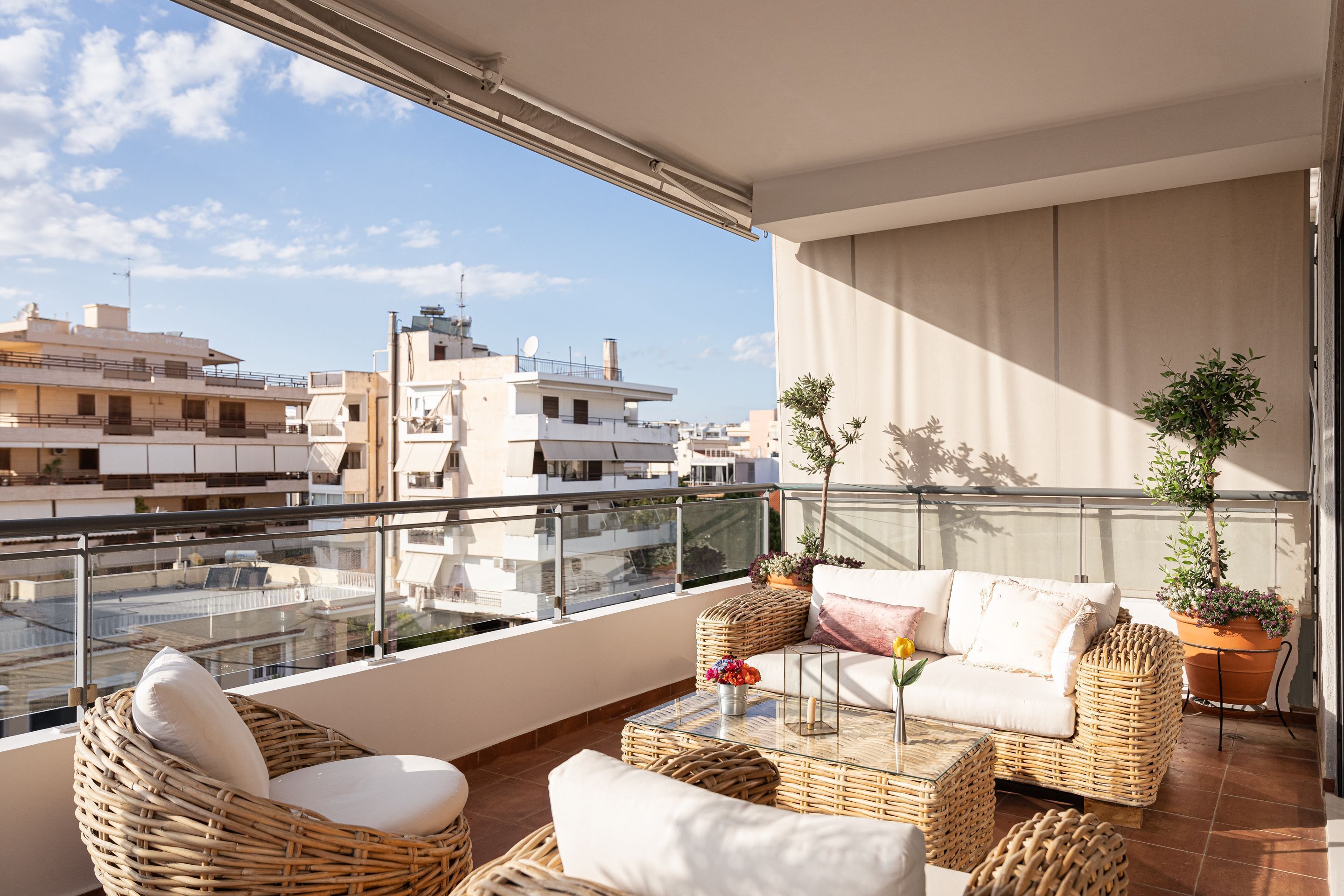 A balcony with wicker furniture, a glass table, and potted plants.