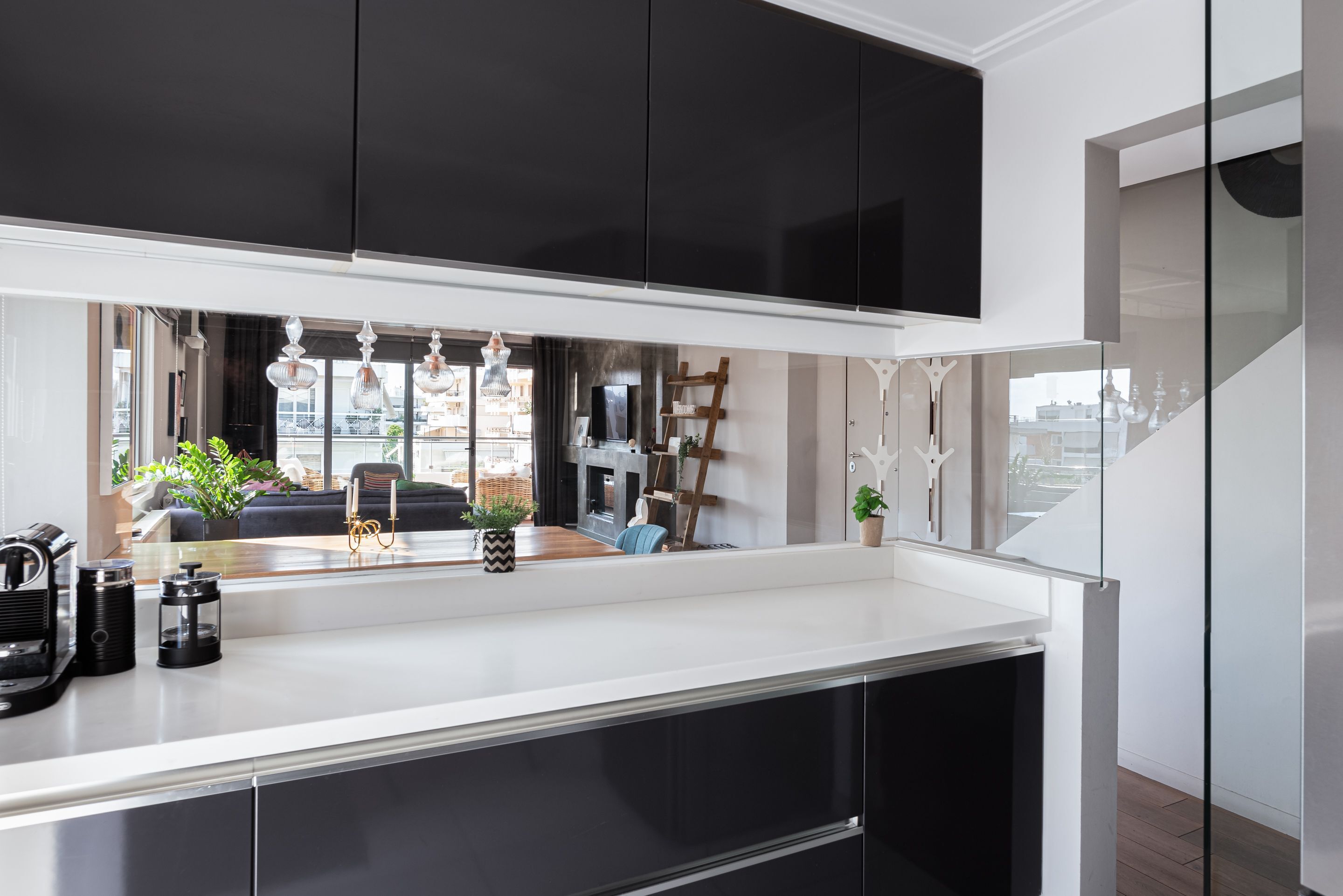 A modern kitchen with dark cabinets, a white countertop, and a view of a living area with a sofa and plants.
