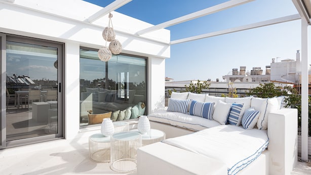A modern outdoor seating area with a white sofa, round tables, and hanging lights. - Glyfada Luxury Living (Glyfada)