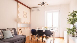 Ein modernes Wohnzimmer mit einem grauen Sofa, einem Esstisch mit vier Stühlen und einem großen Fenster.