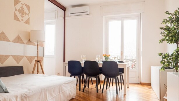 Ein Schlafzimmer mit einem Bett, einem Schreibtisch mit Stühlen, einer Lampe und einem Fenster.