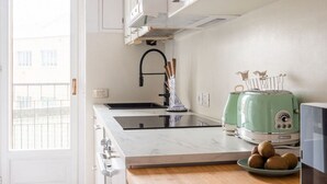 Eine Küche mit weißer Arbeitsplatte, einem Spülbecken, einem grünen Toaster und einem Fenster mit Blick auf Gebäude.