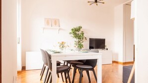 Ein Essbereich mit einem weißen Tisch, vier Stühlen, einer Vase mit Blumen und einem Fernseher auf einem Schrank.