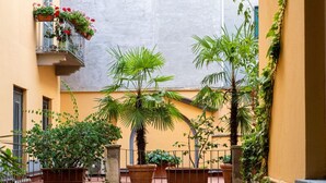 Un pati amb plantes en testos, un balcó amb flors i una paret groga.