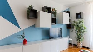 Een moderne woonkamer met een televisie, witte kasten en planten op planken.