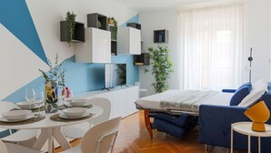 Een moderne, goed verlichte kamer met een bed, een eethoek en ingebouwde planken met planten.