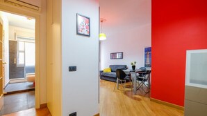 Ein modernes Wohnzimmer mit roter Akzentwand, einem grauen Sofa und einem Essbereich mit Tisch und Stühlen.