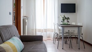 A living room with a sofa, a dining table with chairs, a TV mounted on the wall, and a radiator. - The Best Rent - Modern two bedroom apartment in the Maciachini area (Milano)