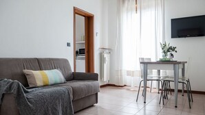 A living room with a grey sofa, a striped pillow, a small table with chairs, and a TV mounted on the wall. - The Best Rent - Modern two bedroom apartment in the Maciachini area (Milano)