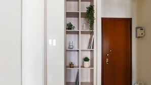 A hallway with a wooden door, a white shelf unit with decorative items, and a magazine holder on the wall. - The Best Rent - Apartment in Piazza Cinque Giornate (Milano)
