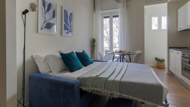 A modern bedroom with a bed, bedside table, and a view of the kitchen. - The Best Rent - Apartment in Piazza Cinque Giornate (Milano)
