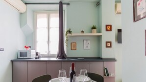 A dining area with a table set for four, a microwave, a wine bottle, and a window with a curtain. - The Best Rent - Lovely one-bedroom apartment in Brera district (Milano)