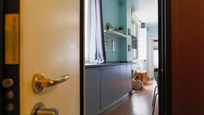 A hallway with grey cabinets, a window with a curtain, and a small table with a plant. - The Best Rent - Lovely one-bedroom apartment in Brera district (Milano)