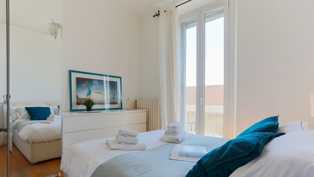 Een moderne slaapkamer met een bed, nachtkastje, spiegel en raam met gordijnen.