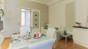 Een moderne woonkamer met een glazen eettafel gedekt voor het ontbijt, een bank, een radiator en een tv op een standaard.