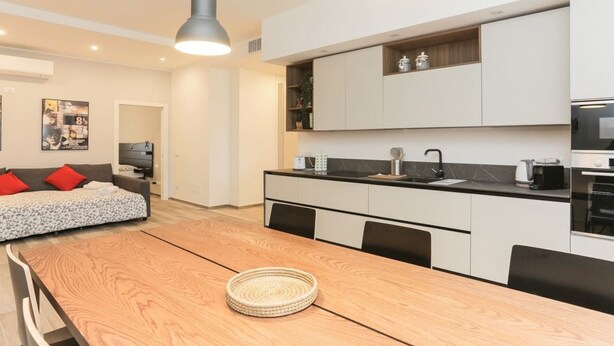Une cuisine moderne avec des meubles blancs, une table à manger en bois et un plan de travail noir.