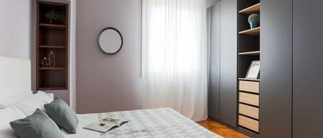 Une chambre à coucher comprenant un lit, une table de chevet, une armoire et une fenêtre avec des rideaux.